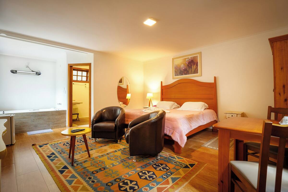 A hotel room with a bed, two chairs, a small table, a rug, and a painting on the wall.