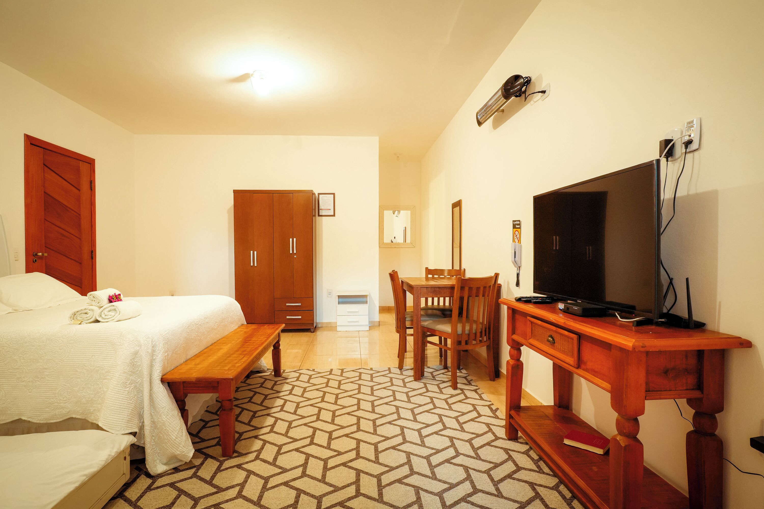 A hotel room with a bed, a wooden desk, a television, and a wardrobe.