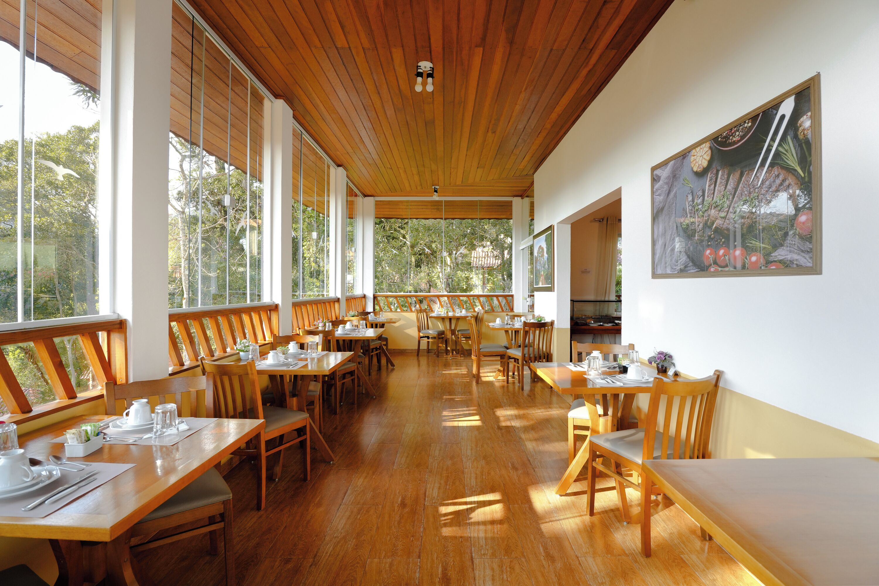 Un vaste espace dédié à la salle à manger, avec des tables et des chaises en bois, de grandes fenêtres et un plafond également en bois.
