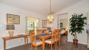 A dining area with a wooden table and chairs, a chandelier, and a potted plant.