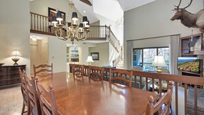 Un vaste espace dédié à la salle à manger, avec une grande table et des chaises en bois, un lustre et une tête de cerf fixée au mur.
