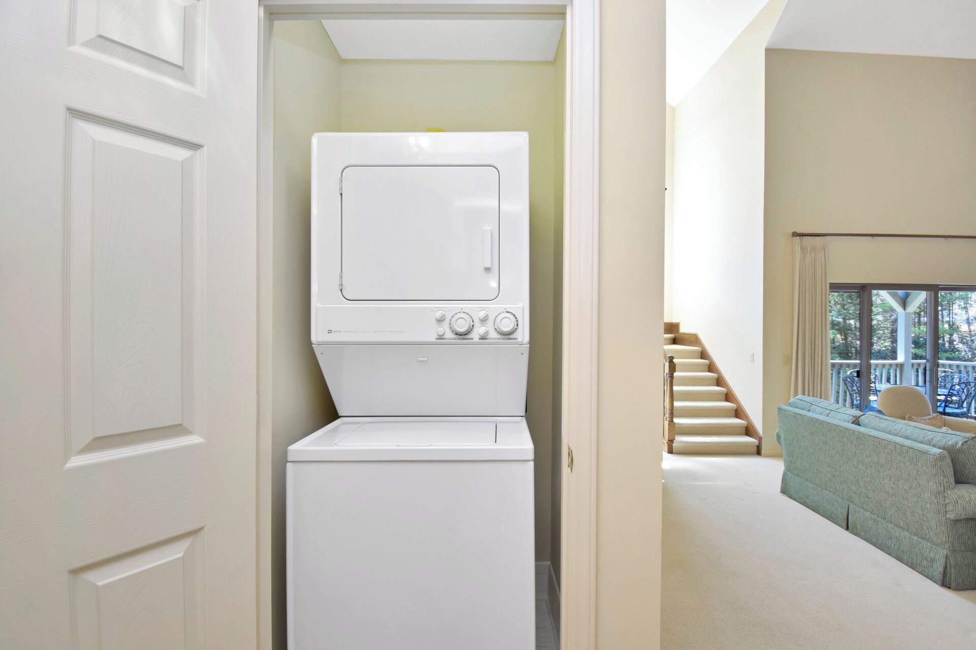 Une buanderie équipée d’un lave-linge et d’un sèche-linge à chargement frontal, d’un escalier menant à un balcon et offrant une vue sur l’extérieur.