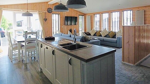 A spacious kitchen with a central island, a dining area with chairs, and a living room with a sofa and cushions.