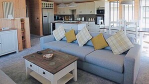A living room with a sofa, coffee table, and a kitchen area in the background.