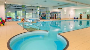 An indoor swimming pool with a circular section, surrounded by tiled flooring and walls, with a staircase leading to an upper level.