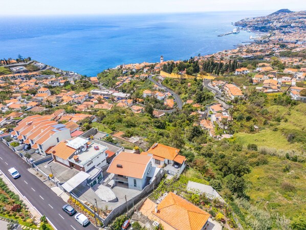 Vista aérea de una zona residencial costera con casas escalonadas, una carretera y un puerto al fondo.