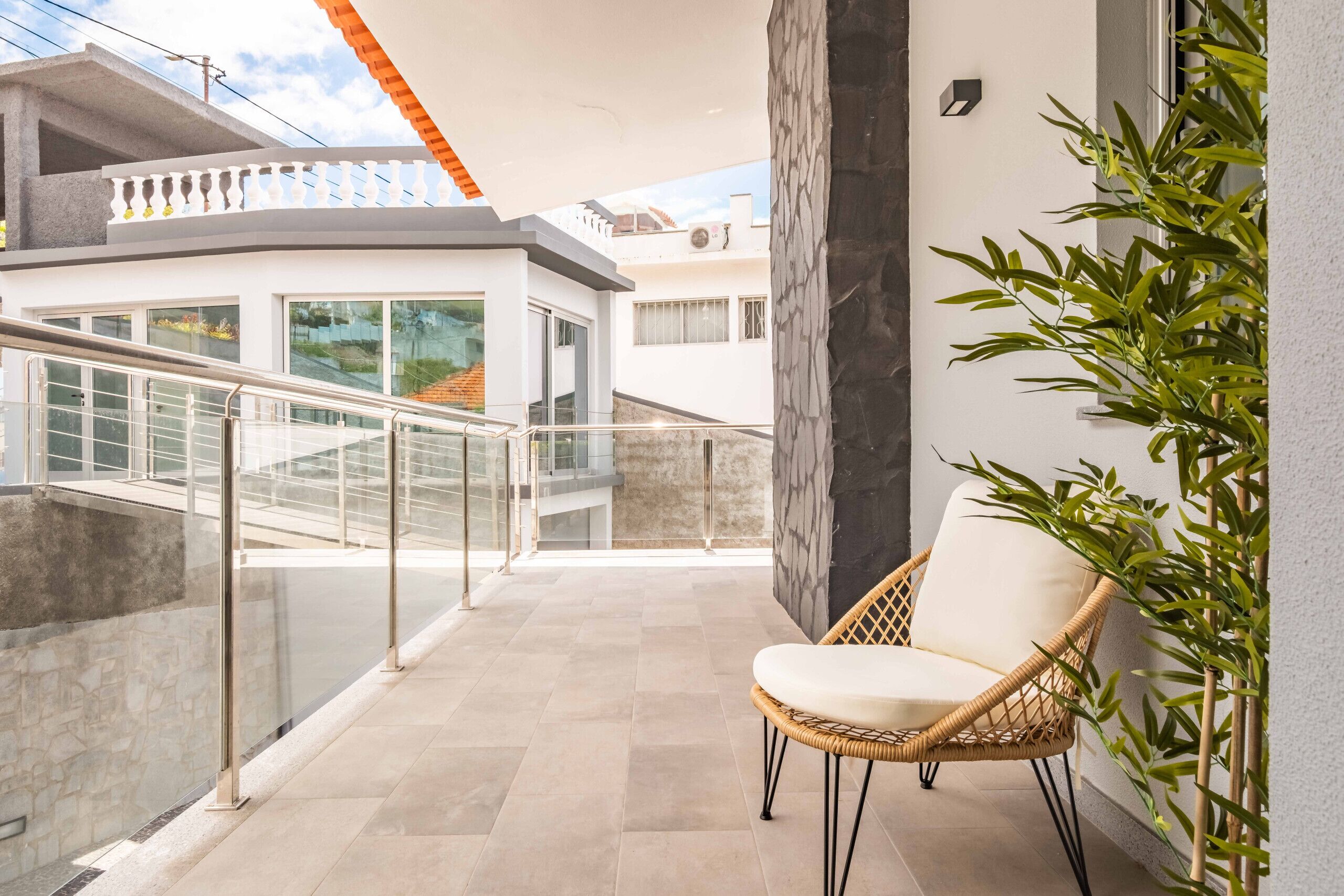 A balcony with a wicker chair, glass railing, and a potted plant.