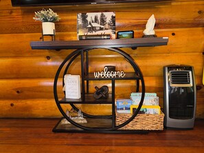 A wooden wall with a shelf displaying a welcome sign, a book, a clock, and a small potted plant.
