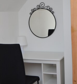 A white desk with a black chair and a round mirror with a decorative black frame.