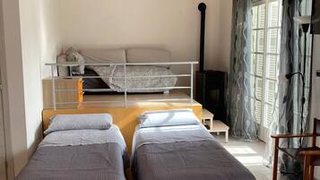 A room with two single beds, a bunk bed, a wooden ceiling, and a window with curtains.