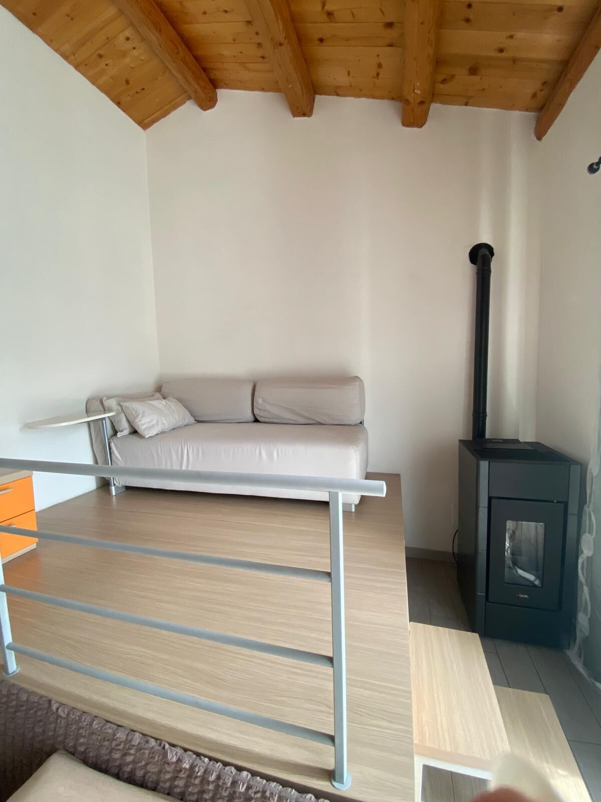 Ein modernes Wohnzimmer mit einer Couch, einer Holzbalkendecke, einem Kamin und einem Metallgeländer.