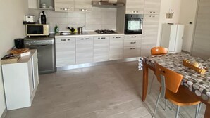 A modern kitchen with light wood cabinets, stainless steel appliances, and a dining area with a patterned tablecloth. - Country house 5 minutes from downtown with garden and private parking space (Abruzzo)