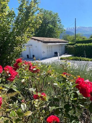 A white building with a tiled roof, surrounded by lush greenery and red flowers.