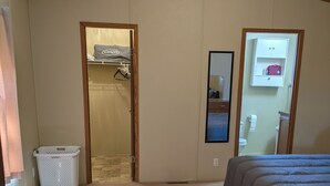 Une chambre à coucher comprenant un lit, un panier à linge blanc, un placard et une salle de bain avec des toilettes et un lavabo.