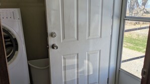 Une buanderie équipée d’un lave-linge, d’une poubelle et d’une porte donnant sur l’extérieur.