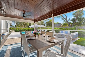 Una veranda coperta con un tavolo da pranzo, sedie in vimini e una piscina sullo sfondo.