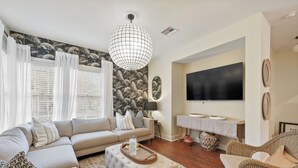 Una sala de estar con un sofá modular, una mesa de centro, un sillón de mimbre, un televisor de pantalla plana y una pared con diseño.