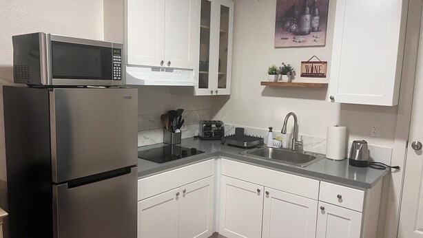 A modern kitchen with white cabinets, a stainless steel refrigerator, a microwave, a sink, and a toaster.