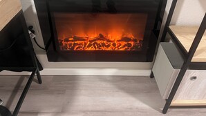 A modern fireplace with a visible fire, surrounded by minimalist furniture and a light-colored floor.