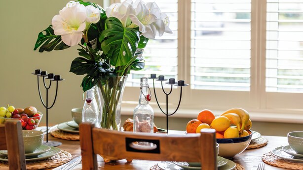 A dining table with a vase of flowers, a bowl of fruit, and a candle holder.