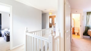 A hallway leading to a bedroom with a white railing, a visible bathroom, and a door with a green curtain.