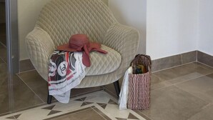 Une pièce avec un grand fauteuil confortable, un sac de la marque Chanel et un sac à rayures posé sur le sol.