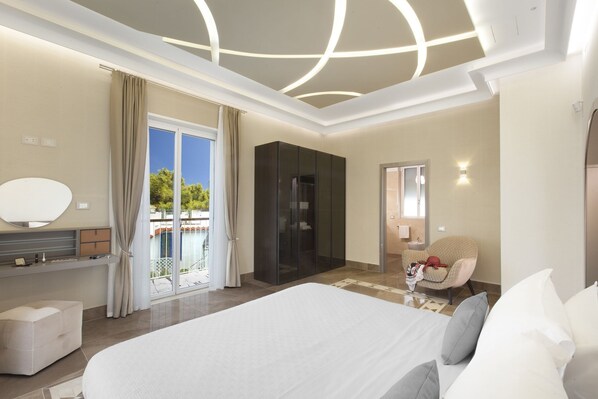 Ein modernes Hotelzimmer mit einem großen Bett, einem Schminktisch mit Spiegel, einem Kleiderschrank und einer Sitzecke mit Sessel und kleinem Tisch.