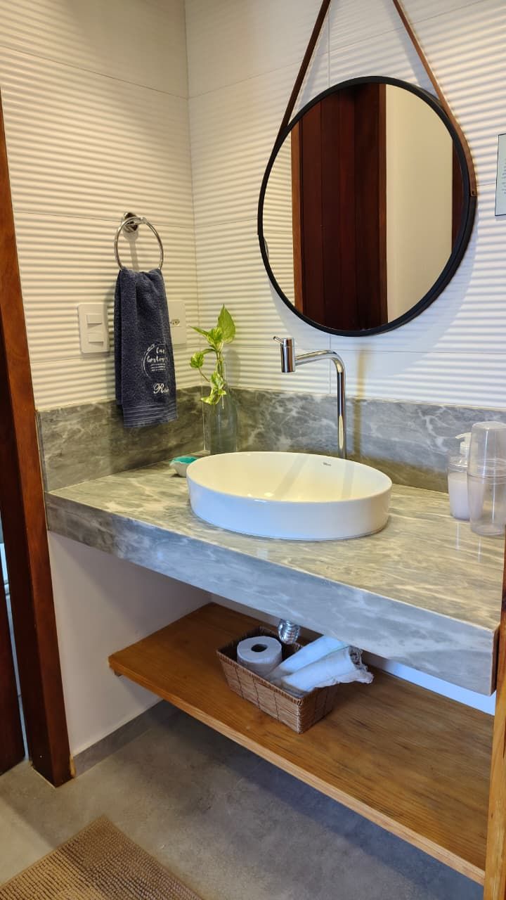 Un baño con un espejo redondo, un lavamanos blanco y una planta pequeña sobre la encimera.