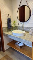 Un baño con un espejo redondo, un lavamanos blanco y una planta pequeña sobre la encimera.