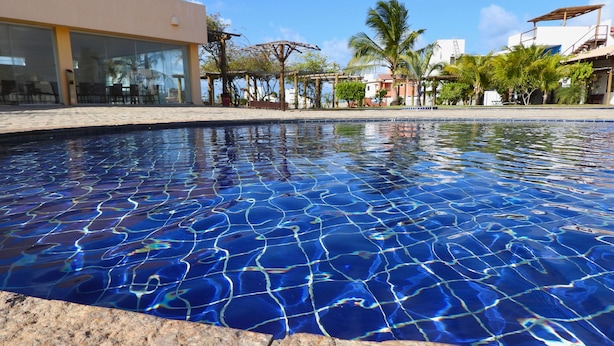 A swimming pool with a clear blue water surface, surrounded by a modern building with large windows and a patio area. - Casa Gostoso Mar (Monte Alegre)