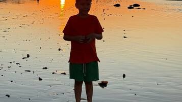 Cena de praia com pôr do sol, mostrando uma pessoa em primeiro plano.