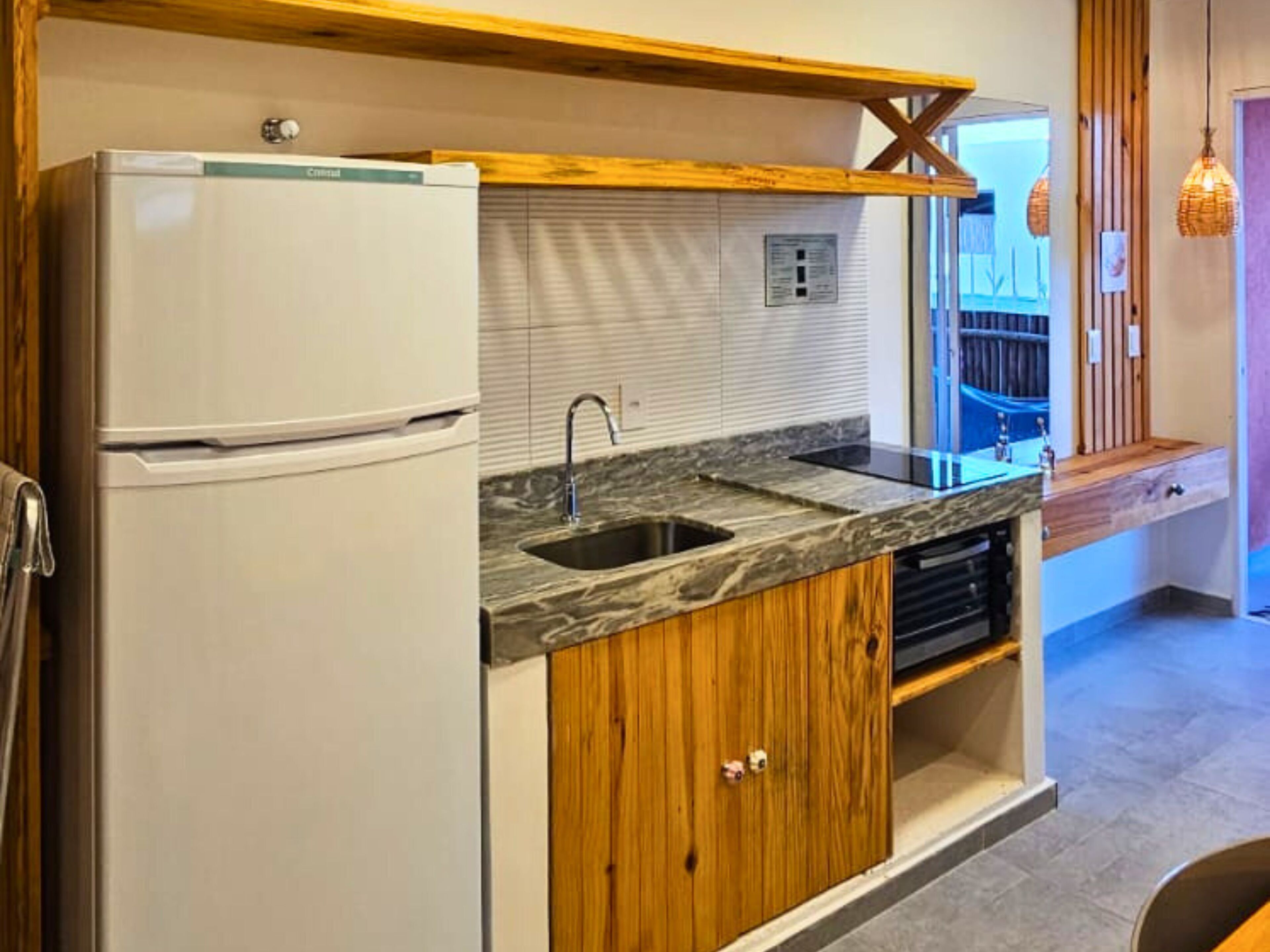 Eine Küche mit einem Einbaukühlschrank, einer Spüle, Holzschränken und einem Fenster mit Jalousien.