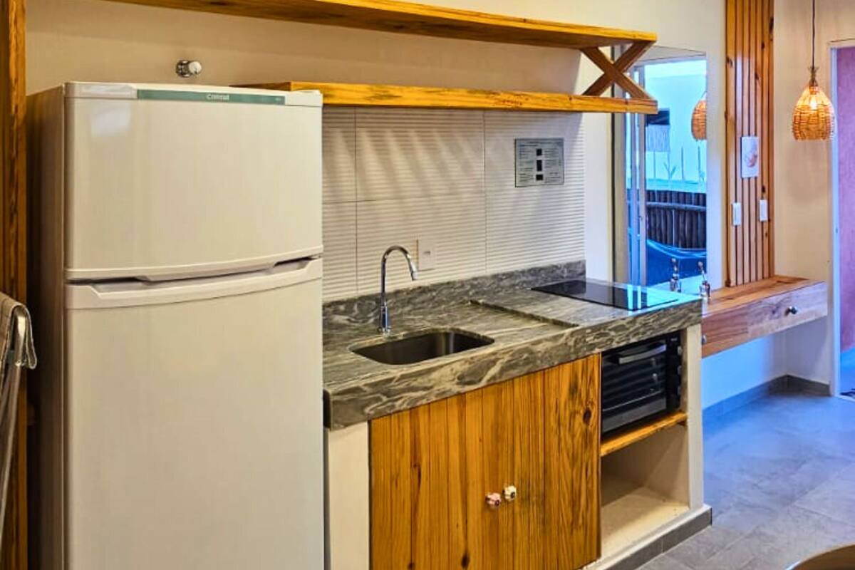 Une cuisine équipée d’un réfrigérateur encastré, d’un évier, de meubles de rangement en bois et d’une fenêtre avec des stores.