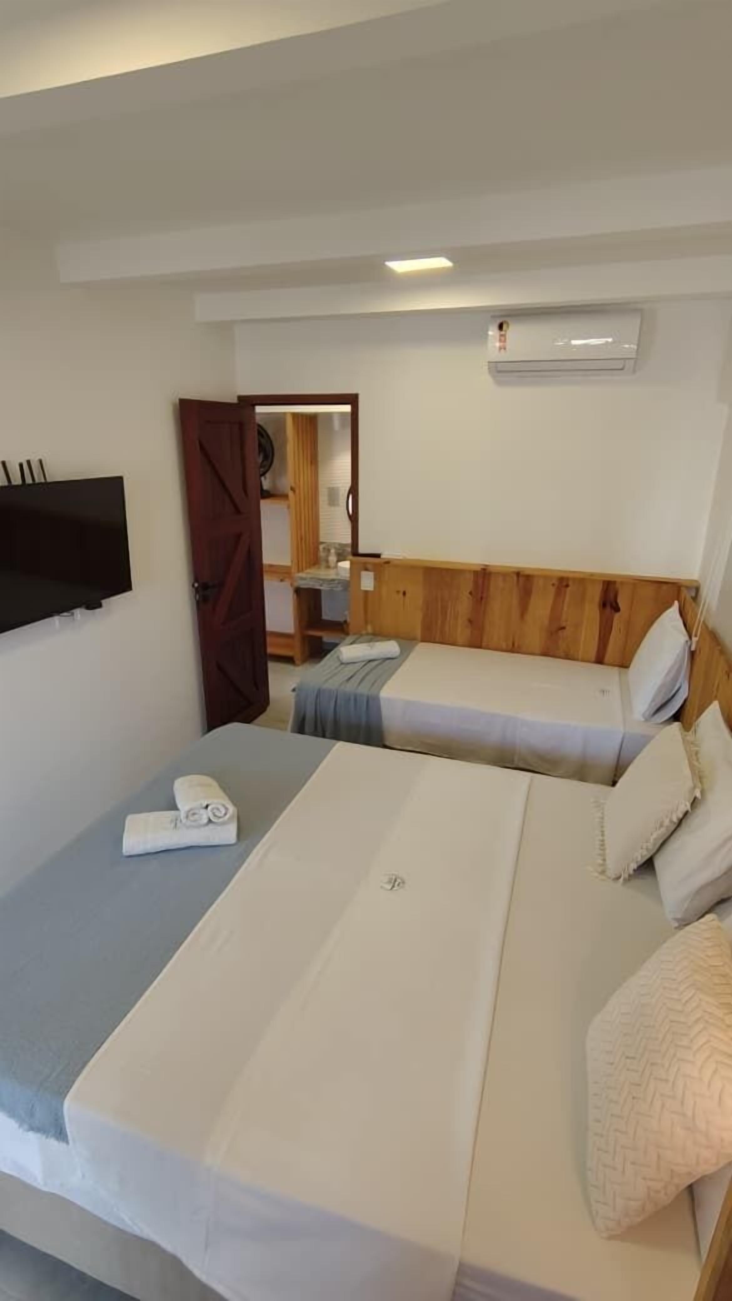 Ein Zimmer mit zwei Betten, einem an der Wand befestigten Fernseher und einer Holztür.