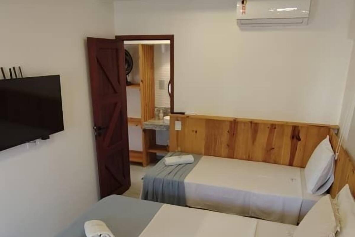 Une chambre avec deux lits, un téléviseur fixé au mur et une porte en bois.