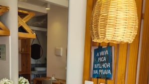 A reception desk with a mirror, a woven light fixture, a blue sign with Portuguese text, and a wicker basket with a blue bag. - Casa Gostoso Mar (Monte Alegre)