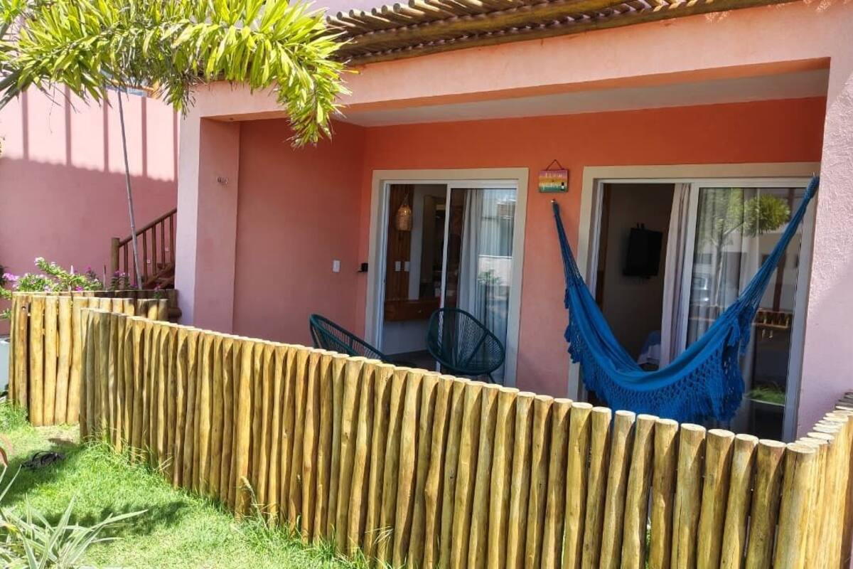 Un bâtiment rose avec une clôture en bois, un hamac et une chaise à l’extérieur.