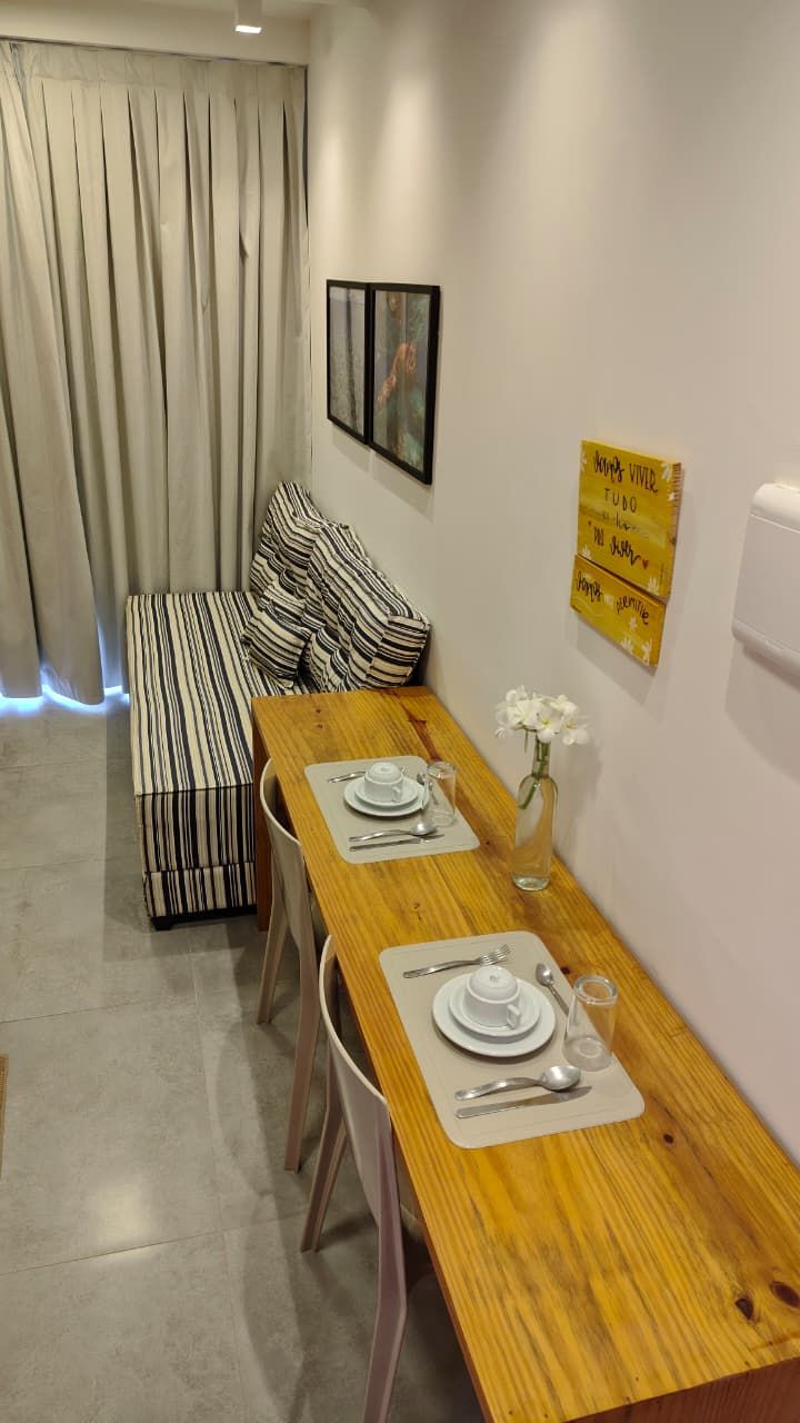 A dining area with a wooden table set for two, a bench with striped cushions, and a yellow sign on the wall.