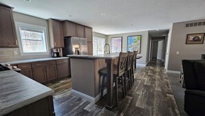 A modern kitchen with dark wood cabinets, a stainless steel refrigerator, and a central island with bar stools. - Newly built secluded home, large game room, full RV hook-up (Mears)