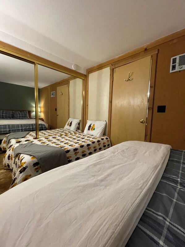Two single beds with white linens and a patterned duvet cover, a wooden wardrobe, and a door with a handle.