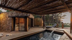 A wooden deck with a hot tub, stone walls, and a covered area with a wooden roof.