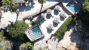An aerial view of a resort with a pool, lounge chairs, and rocky terrain.