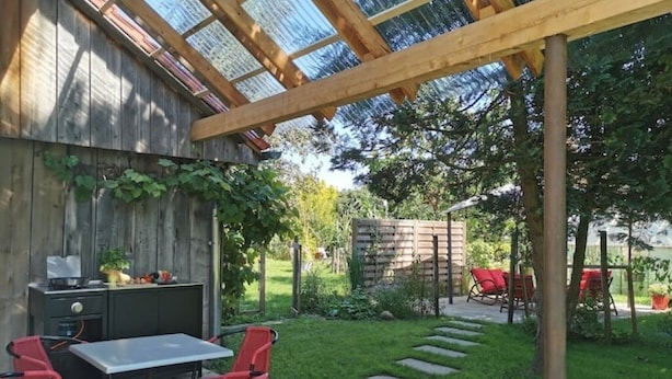 A patio with a wooden pergola, a table, and red chairs.