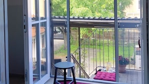A room with a sliding glass door leading to a balcony with a red rug, a small table, and a chair.