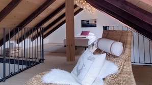 A cozy attic bedroom with a sloped ceiling, a wicker sofa bed, a small bedside table, and a framed picture on the wall.