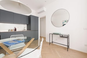 A modern kitchen with grey cabinets, a round mirror, a glass table with a magazine, and a small black table with a glass top. - Brera Apartments In Garibaldi (Milan)