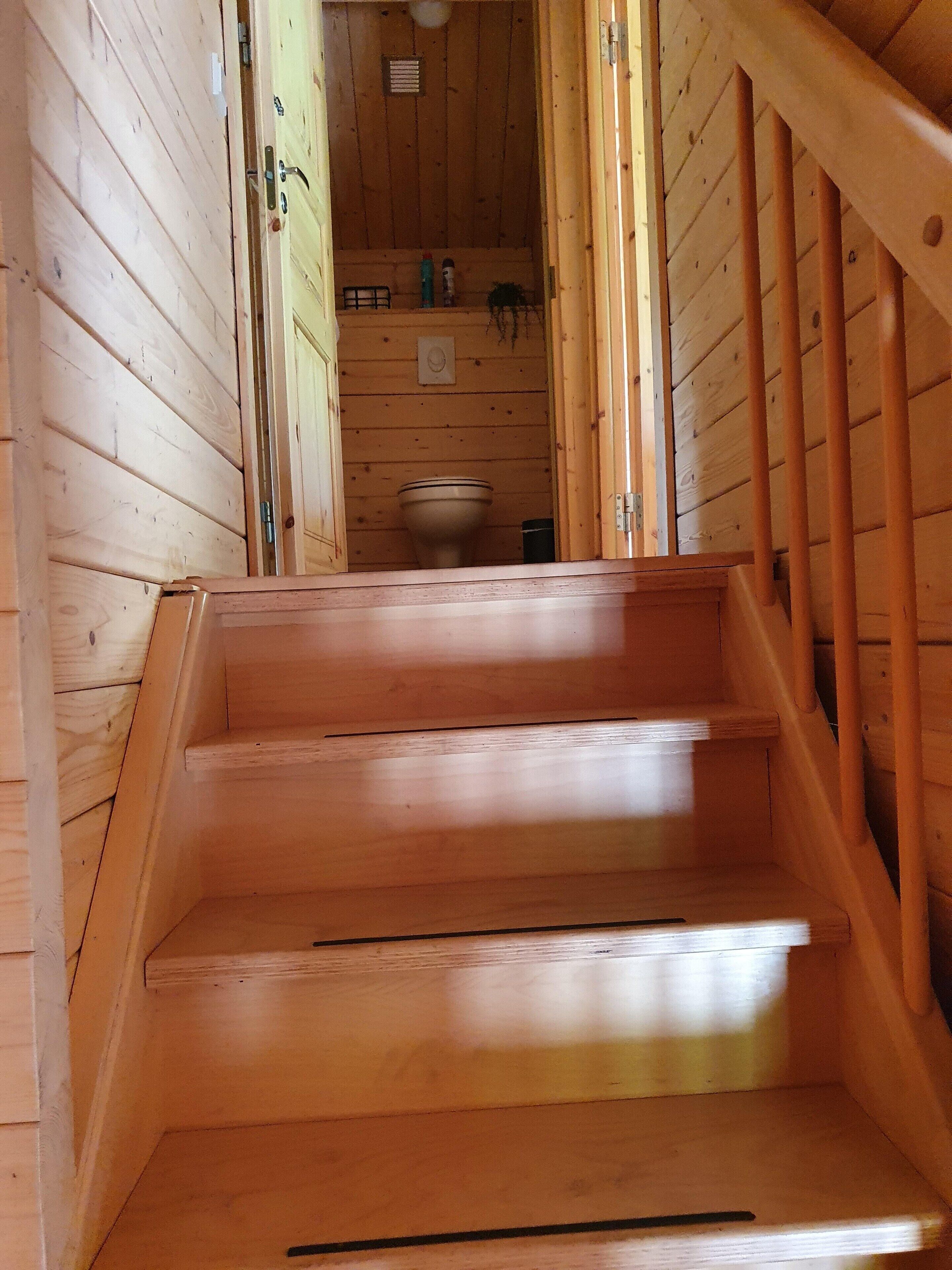 Una escalera de madera que conduce a un baño con un inodoro y un pequeño estante con artículos de aseo.