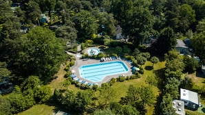 Vue aérienne d’un quartier résidentiel avec une piscine entourée d’arbres et de maisons.