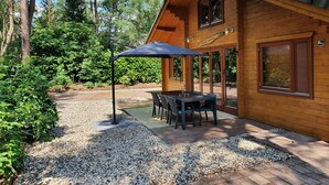 Une cabane en bois dotée d’une terrasse, d’une table avec des chaises et d’un espace salon couvert avec un parasol.