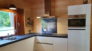 Une cuisine moderne avec des murs en bois, un plan de travail noir, des armoires blanches, une hotte de cuisine en acier inoxydable et un four encastré.
